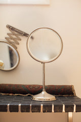 Antique standing shaving mirror with circular beveled glass and time-softened silver tones.