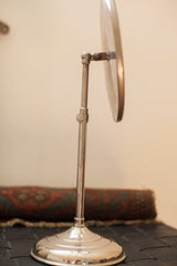 Silver-toned metal base and adjustable stand of an antique shaving mirror, with natural patina.