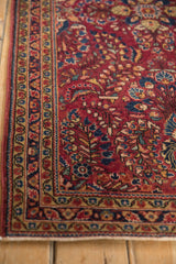 Corner view of the Sarouk rug's serrated leaf and vine borders in raspberry, blue, and gold.