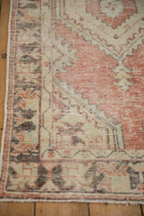 Distressed Oushak rug corner showing worn texture in faded brick red and ivory.
