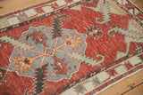 Distressed Oushak rug corner showing serrated gray-blue spandrel and geometric vine border in cherry red.