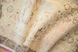Mostly even wear across the hand-knotted pile of a distressed Oushak rug in sandalwood tones.