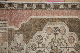 Detail of the worn, low pile on a vintage Oushak rug corner with floral motifs in olive and mauve.