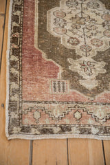 Corner detail showing the worn low pile, faded mauve border, and bronze scalloped medallion.