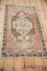 Angled view of a vintage distressed Oushak rug with olive, bronze, and mauve tones.