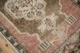 Angled view of the distressed Oushak rug's corner showing low pile and the faded mauve border.
