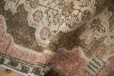 A detailed view of a distressed vintage Oushak rug folded to show the low pile and knot heads.