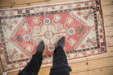 A person's view looking down at a distressed vintage Oushak rug with a geometric pattern.