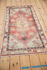Angled view of a distressed Oushak rug showing the faded brick red and charcoal geometric pattern.