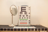 Vintage Graham Field eye exam light box displaying black E chart with green and red lines.
