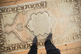 Vintage distressed Oushak rug with a scalloped medallion, shown from a standing perspective for scale.