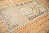 Angled view of a distressed Oushak rug, showing its scalloped medallion and time-softened beige tones.