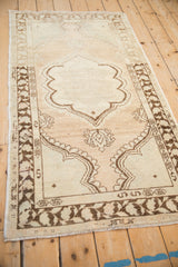 Full length view of a vintage distressed Oushak rug with a chocolate brown medallion on an abrashed beige ground.