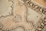 The abrashed beige field and chocolate brown serpent border of a vintage distressed Oushak rug.