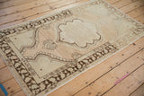Angled view of a vintage Oushak rug highlighting its distressed wear and soft neutral tones.
