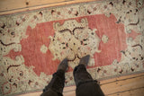 A person standing on a distressed vintage Oushak runner, highlighting its scale and soft, dusty red tones.