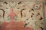 Corner detail of the distressed Oushak rug showing even wear over pale brick red and beige floral motifs.