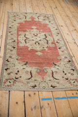 Angled view of a vintage Oushak runner's distressed texture and brick red and sand colored pattern.