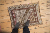 Distressed Kars rug with worn pile, geometric patterns, and checkered borders in aubergine and ivory.