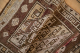 Distressed Kars rug's hand-knotted pile with worn geometric patterns in aubergine, brown, and ivory.