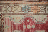 Geometric floral border in tangerine and teal showing the distressed, low pile of the rug.