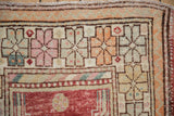 Close-up of a distressed Oushak rug corner with geometric pinwheel florals in tangerine and seafoam.