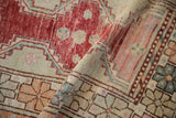 Low pile texture of a vintage Oushak rug with raspberry floral and seafoam geometric patterns.