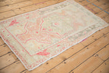 Angled view of a distressed Turkish Oushak rug with a central shield medallion and a faded pastel palette.