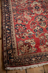 Intricate navy vine border and intact side cord selvage of a vintage red Persian Sarouk rug.