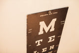 Top corner of antique Snellens test types hanging, white letters on black board, edge peeling.