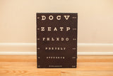 Antique Snellen eye chart showing white letters on black heavy board with aged edges.