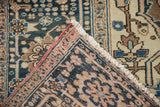Folded corner of distressed Heriz carpet, showing hand knotted back, ivory fringe, and rosy selvage.
