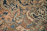 Distressed texture and sprawling floral details of a vintage Heriz carpet in rose, navy, and brown.