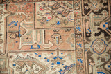 Distressed vintage Heriz carpet's geometric patterns in dusty rose, brown, and royal blue.