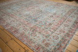 Distressed Persian Meshed rug showing worn floral motifs, faded raspberry border, powder blue tones.
