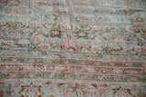 Distressed vintage Persian Meshed carpet detail: worn pile, exposed foundation, faded floral border.
