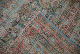 Textured distressed Meshed rug corner with faded floral border and blue fringe.