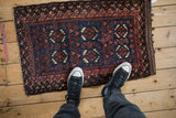 Antique Belouch rug mat shown for scale, highlighting its geometric medallions on a deep cobalt blue field.
