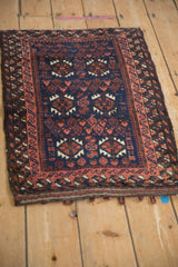 Angled view of an antique Belouch rug with a cobalt blue field and dusty red geometric borders.