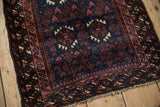 Corner view of an antique Belouch mat showing its pawn design and ribboned serpent borders in red and blue.