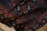 A folded corner on the antique Belouch rug shows its soft hand-knotted pile and pawn design motif.