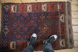 Person standing on an antique Belouch rug, providing scale for the geometric ram's horn design.