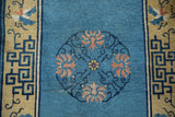 Antique Peking rug detail: sky blue field, dusty rose quatrefoil lotus, geometric border, visible foundation.