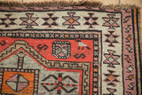 Vintage Caucasian rug corner displaying geometric patterns in tomato red, ivory, mauve, and chocolate brown, with fringe.