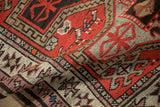 Close-up of hand-knotted Caucasian rug pile with geometric red, ivory, and brown patterns.