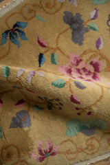 The plush, mostly even pile of an antique Art Deco rug showing gold, mauve, and blue florals.