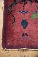 Antique Art Deco rug corner shows cochineal red field, aubergine border, tattered fringe.