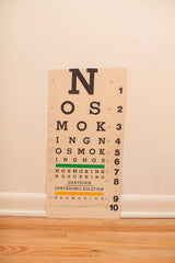 Close-up of vintage eye chart bottom with 'Nosmoking' text, Gantrisin, and torn edge.