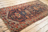 Antique Persian Malayer rug runner's tattered end, revealing worn geometric patterns.