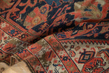 Antique Malayer rug's geometric border and worn field, featuring blue, red, and gold tones.